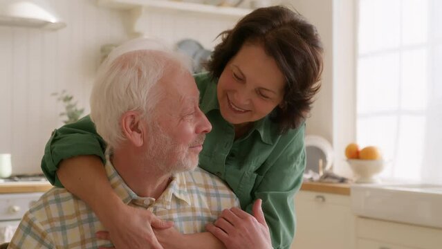 close up view of elderly woman comes up to her husband and embraces him, smiling. Impact of dementia on relationships. Tender moments in old age.