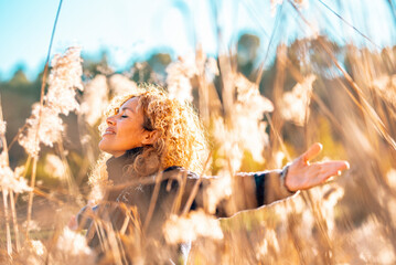 One happy woman outstretching arms in a high yellow grass field in sunset golden sunlight smiling and breathing to enjoy nature and love environment and sustainability. People female success lifestyle