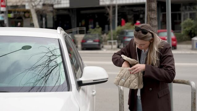 Young nervous businesswoman searching for car keys in her purse standing near vehicle lost the entrance door key while key-less sensor system is out of batteries Female lost and searching in her bag