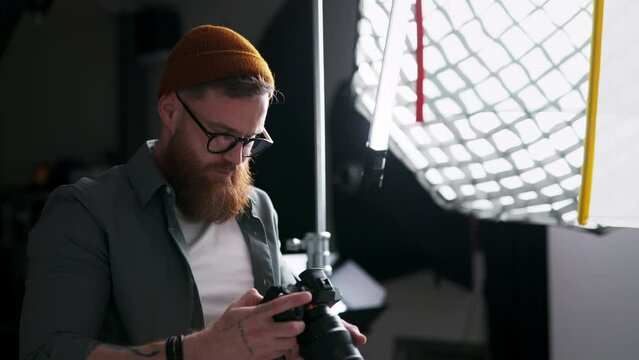 Bearded young photographer man using camera while making pictures at photo studio
