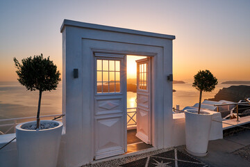 Beautiful sunset seen through an open white door overlooking the sea and Caldera, Santorini,...