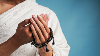Muslim man wearing ihram clothes is praying with prayer beads in his hands