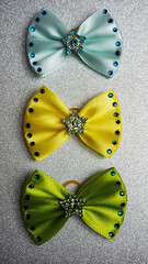 On a silver shiny background lie three bows of turquoise yellow and green with star-shaped inserts with stones. hair accessories. for dogs. top notes. view from above
