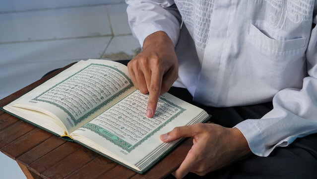 close up photo of a Muslim man reading the Quran on a prayer mat during the holy month of Ramadan.