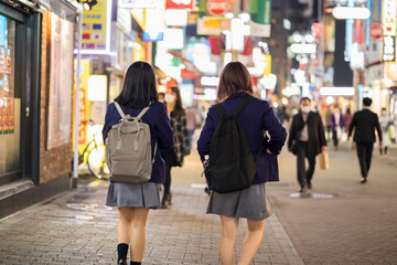 夜の渋谷センター街を歩く制服の女子高生の後ろ姿 - obrazy, fototapety, plakaty