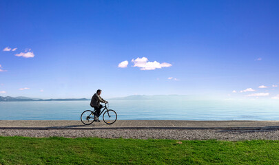 Man riding a bike by the sea, blue sky, sunny day