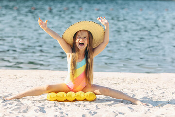 Happy cute smiling little girl in straw hat has fun on the sand on a beach in a swimsuit. Summer...