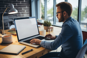Side view of young businessman in eyeglasses using laptop while sitting at table in office