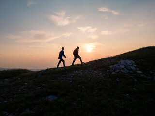 Two teenage hikers walking uphill enjoying a spectacular view while the sun is setting down on the horizon. Active adolescents and nature experience concepts.