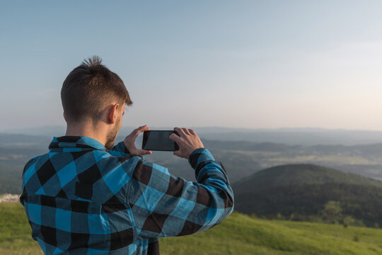 Adolescent boy taking photos of fantastic mountain landscape at sunset with smartphone