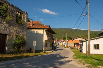 Fototapeta na wymiar A quiet residential road in Kulen Vakuf village in the Una National Park with a derelict house on the left. Una-Sana Canton, Federation of Bosnia and Herzegovina. Early September