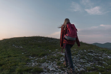 Naklejka na ściany i meble Female hiker silhouette with a backpack walking and following the trail uphill, enjoying the sky at sunset. Inspiration and healthy lifestyles concepts.