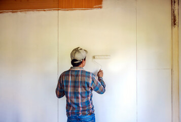 Back view of Workers painter are painting the wooden walls of the room white with paint roller,improvement home interior concept. - obrazy, fototapety, plakaty