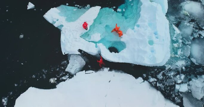 People explore global warming issue in Antarctica. Group of scientists in orange wetsuits take samples and measure melting glacier water, climate change problem. Aerial top down zoom out drone shot