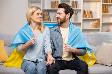 Happy man and woman sit on their sofa with Ukrainian flag, showing solidarity with their country