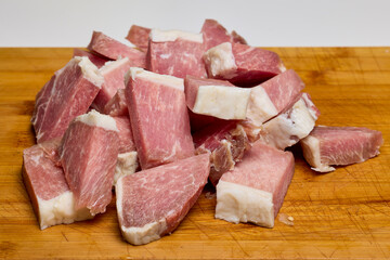 Pork on a wooden chopper cut into pieces to be cooked.