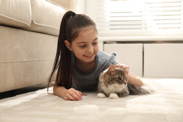 Cute little girl with cat lying on carpet at home. First pet