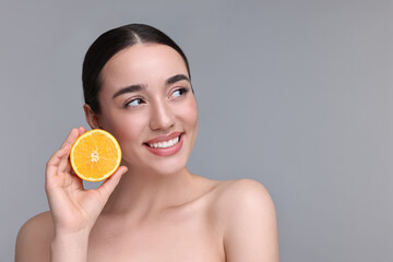 Beautiful young woman with piece of orange on grey background. Space for text