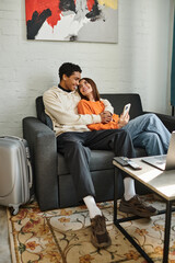 happy diverse couple cozily lounges on a couch in their stylish living room surrounded by gadgets