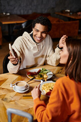 A couple enjoying a cozy meal together, black man showing smartphone to girlfriend