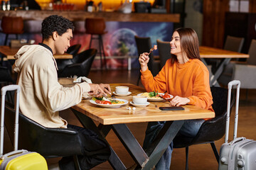 Fototapeta na wymiar diverse couple sharing a joyful moment over a healthy meal in a trendy cafe, travel luggage
