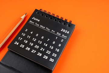 June 2024 desk calendar with pencil on orange background.