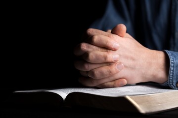 Hands of person folded for pray with Holy Bible