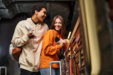 happy black man talking to cheerful woman holding credit card at reception counter in hostel