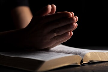Hands of person folded for pray with Holy Bible