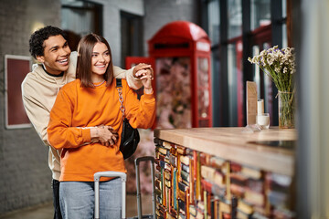 A smiling woman and man stand together at hostel reception desk, holding hands during check in