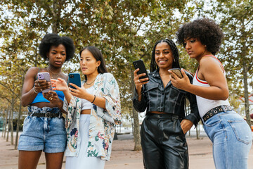 Female friends using phone standing in an urban park