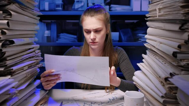 Exhausted young business woman office employee at the desk working late at night overloaded with paperwork. Female frustrated crumpling documents throws them away.