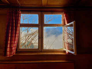 Holzfenster, Scheibe geöffnet, spiegelung der Bäume, blauer Himmel, rot-karierte Vorhänge hängen an den Seiten