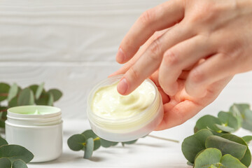 Jar of moisturizing cosmetic cream for face, hands and body in women's hands with eucalyptus leaves...