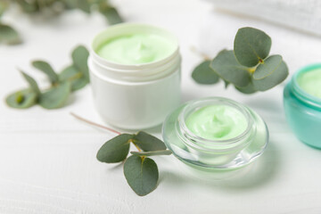 Obraz na płótnie Canvas Jar of moisturizing cosmetic cream for face, hands and body with eucalyptus leaves on a white wooden background. Natural organic product. Beauty and spa concept. Body care. Space for text.Copy space.