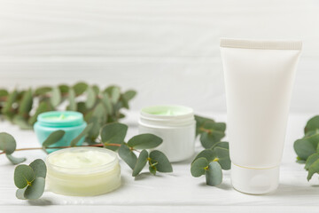 Jar of moisturizing cosmetic cream for face, hands and body with eucalyptus leaves on a white wooden background. Natural organic product. Beauty and spa concept. Body care. Space for text.Copy space.