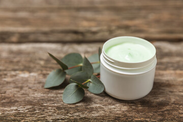 Obraz na płótnie Canvas Jar of moisturizing cosmetic cream for face, hands and body with eucalyptus leaves on brown wooden background. Natural organic product. Beauty and spa concept. Body care. Space for text.Copy space.