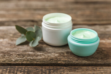 Obraz na płótnie Canvas Jar of moisturizing cosmetic cream for face, hands and body with eucalyptus leaves on brown wooden background. Natural organic product. Beauty and spa concept. Body care. Space for text.Copy space.