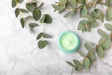 Jar of moisturizing cosmetic cream for face, hands and body with eucalyptus leaves on marble...