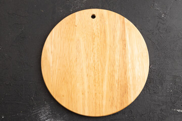 Empty round wooden cutting board on black concrete. Top view