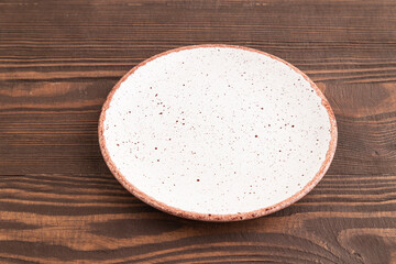 Empty white ceramic plate on brown wooden background. Side view, copy space