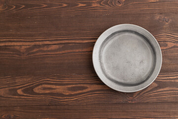 Empty gray ceramic plate on brown wooden background. Top view, copy space