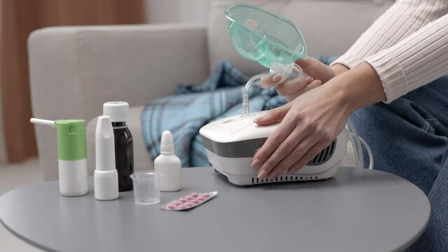 Close-up of sick woman with an inhaler. Unhealthy girl presses the button on the inhaler to inhale, she use nebulizer and inhaler for the treatment sitting on the couch at home