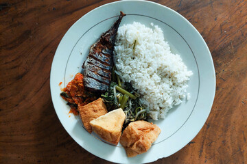 rice mixed with fried fish and tempeh vegetables on a white plate