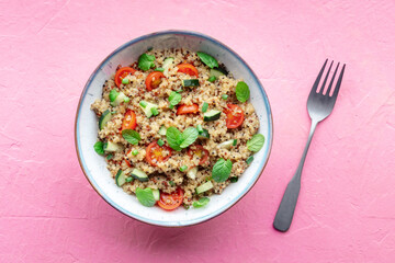 Quinoa tabbouleh salad in a bowl, a healthy dinner with tomatoes and mint, with a fork, overhead flat lay shot