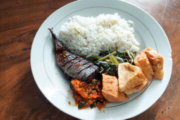 rice mixed with fried fish and tempeh vegetables on a white plate