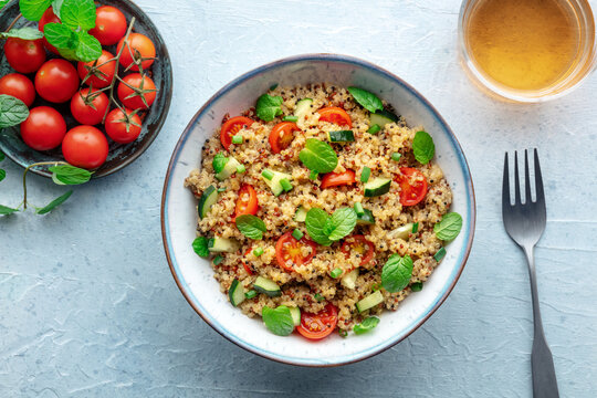 Quinoa tabbouleh salad in a bowl, a healthy dinner with tomatoes and mint, overhead flat lay shot on a blue background