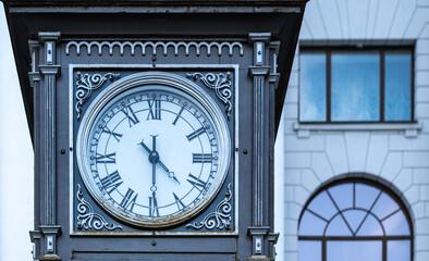 An antique clock with Roman numerals on the street on a pedestal.