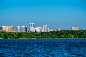 New high-rise buildings on the shore of a lake with a forest.