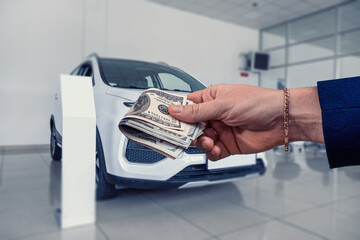 Businessman holding cash in the hand stand at in the showroom with new car